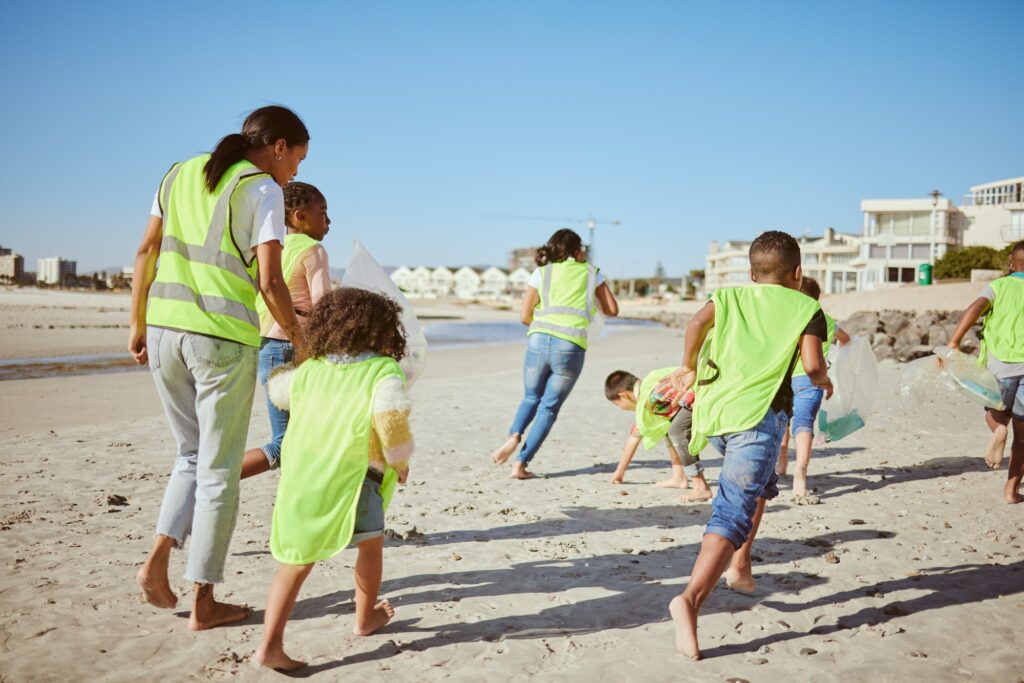 Woman and group of children cleaning beach for volunteering, community and charity with earth day,